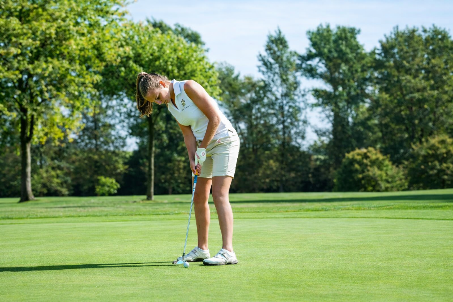 Golfeuse concentrée sur son putt, sur un green entouré d'arbres
